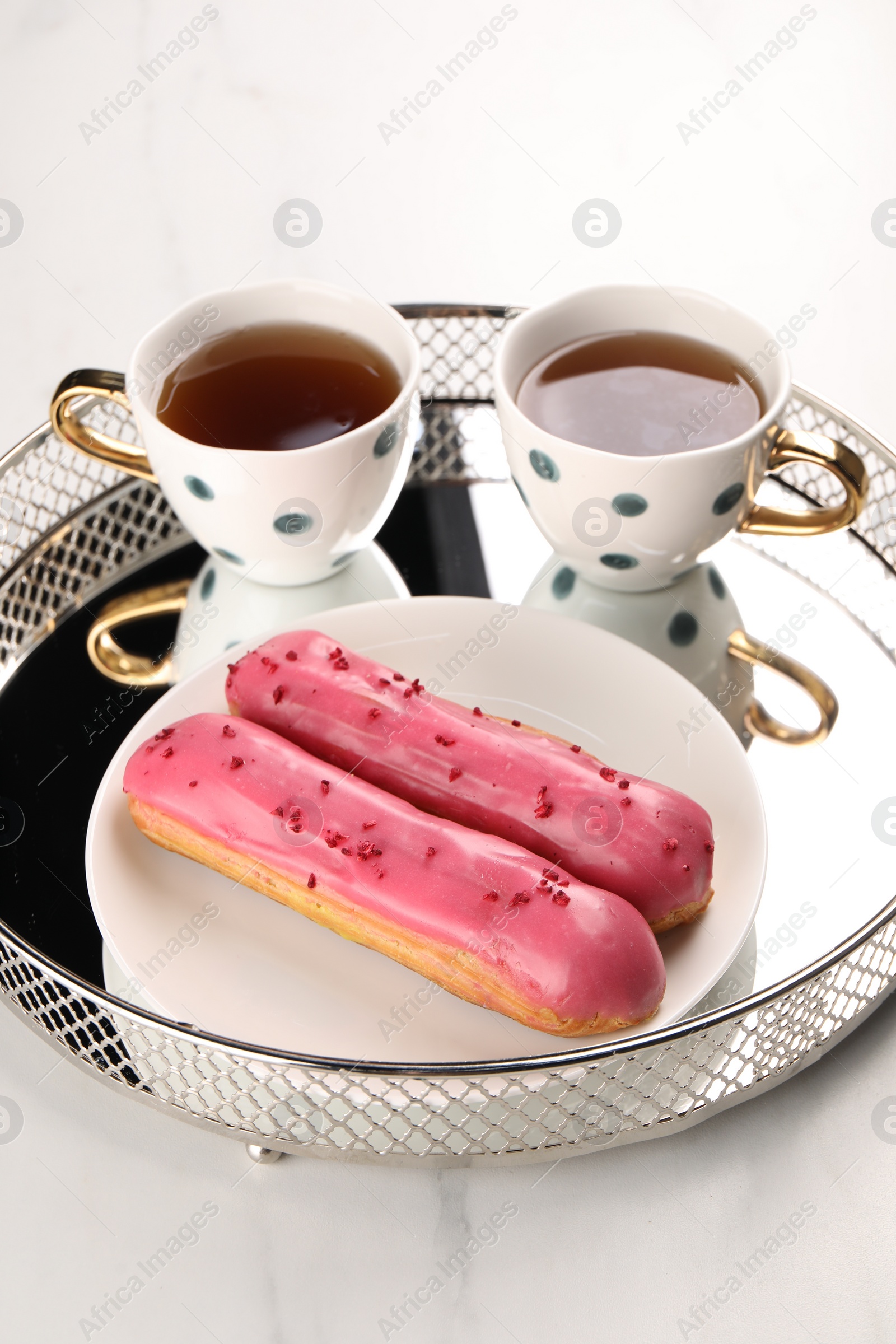 Photo of Tray with tasty glazed eclairs and tea on white table