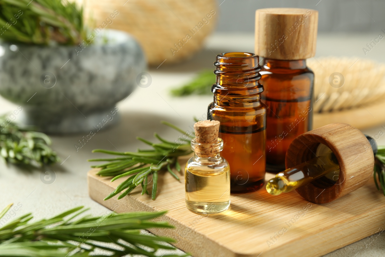 Photo of Essential oils in bottles and rosemary on light gray table, closeup