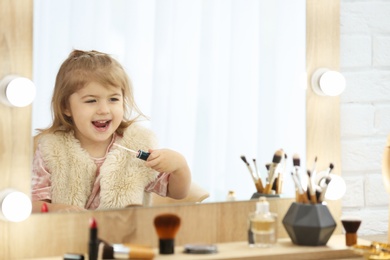 Photo of Cute little girl playing with cosmetics in dressing room