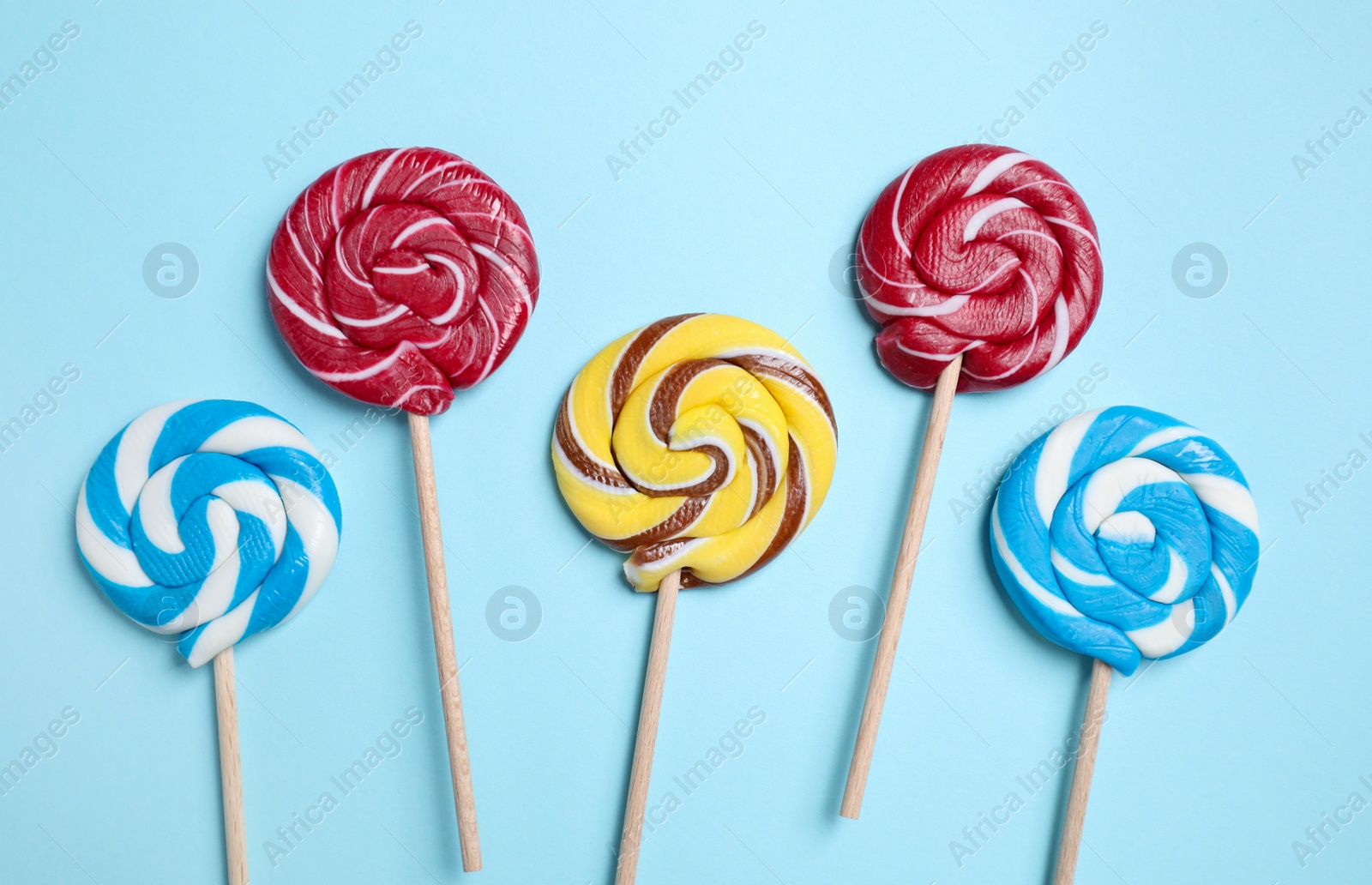 Photo of Sticks with colorful lollipops on light blue background, flat lay