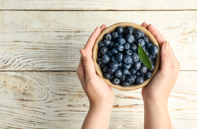 Photo of Woman holding juicy fresh blueberries at white wooden table, top view