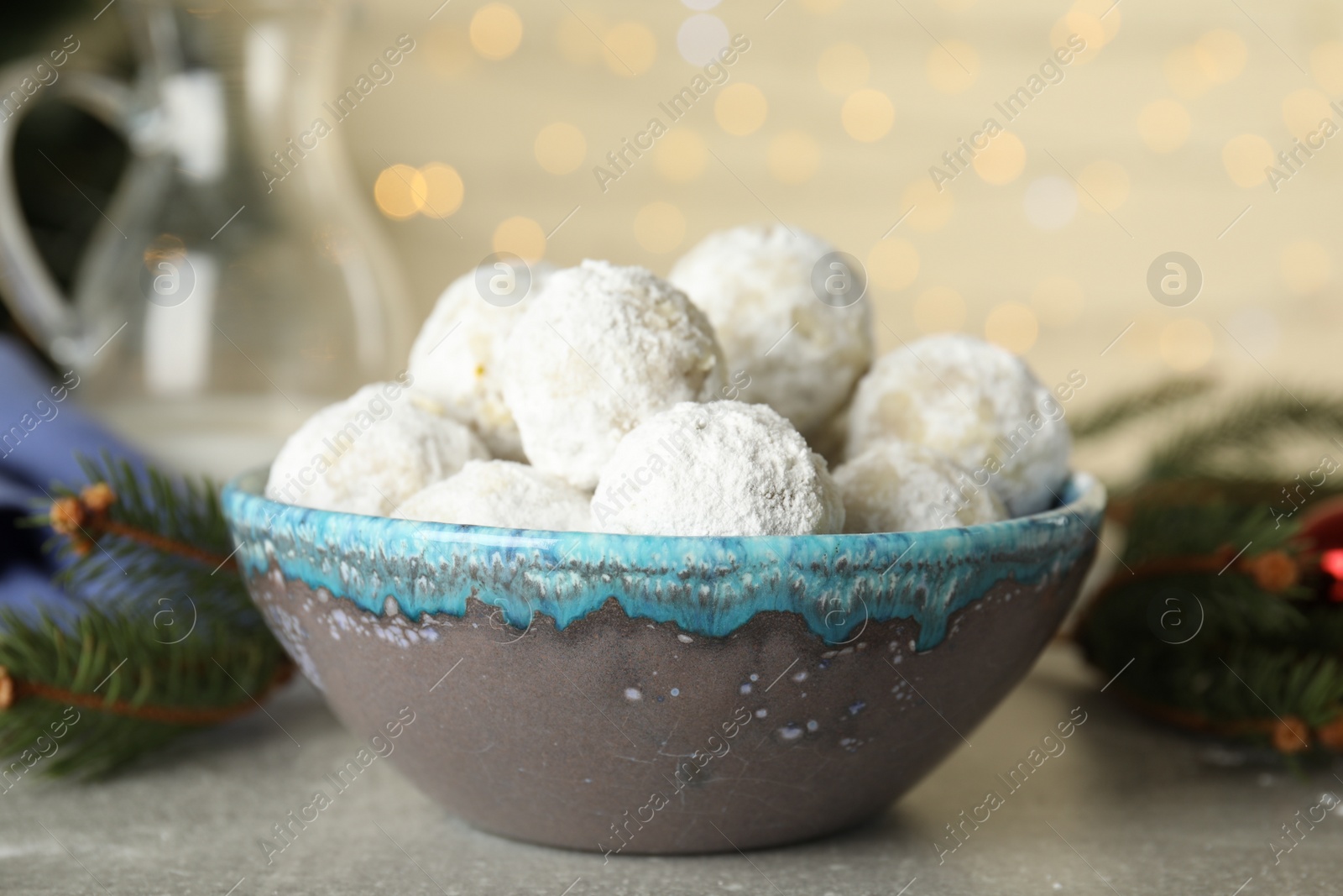 Photo of Tasty snowball cookies in bowl against blurred festive lights. Christmas treat
