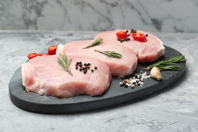 Photo of Pieces of raw pork meat, chili pepper and spices on grey textured table