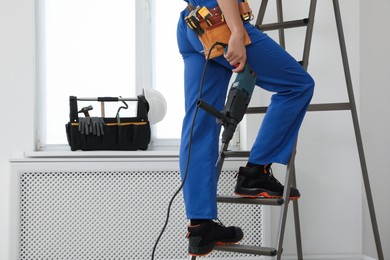 Photo of Worker with electric drill on ladder indoors, closeup