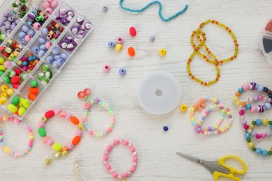 Photo of Beautiful handmade beaded jewelry and supplies on white wooden table, flat lay