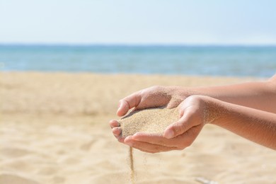 Photo of Child pouring sand from hands on beach near sea, closeup with space for text. Fleeting time concept