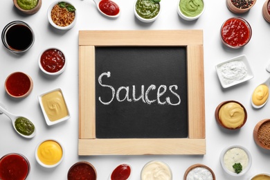 Small blackboard with word Sauces and different dressings on white background, flat lay