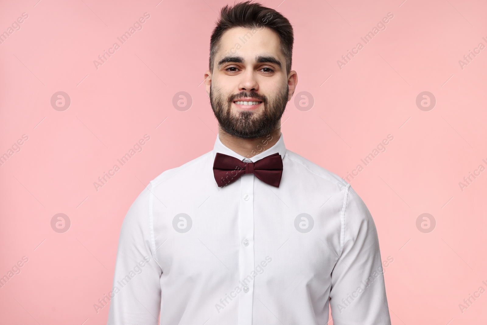 Photo of Portrait of smiling man in shirt and bow tie on pink background