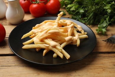 Delicious French fries with cheese sauce, tomatoes, dill and parsley on wooden table, closeup