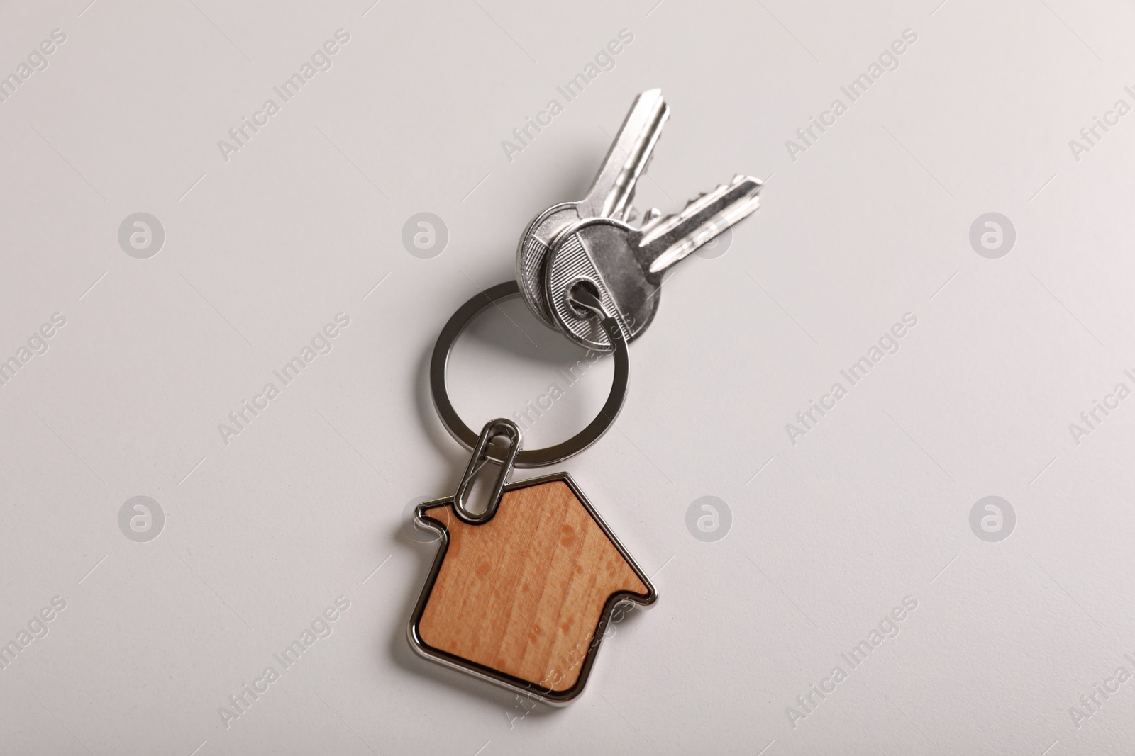 Photo of Keys with trinket in shape of house on white background, top view. Real estate agent services