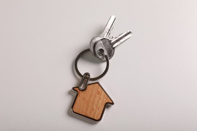 Keys with trinket in shape of house on white background, top view. Real estate agent services