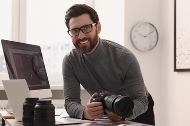 Photo of Professional photographer holding digital camera near table with laptop in office