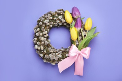 Wreath made of beautiful willow, colorful tulip flowers and pink bow on purple background, top view