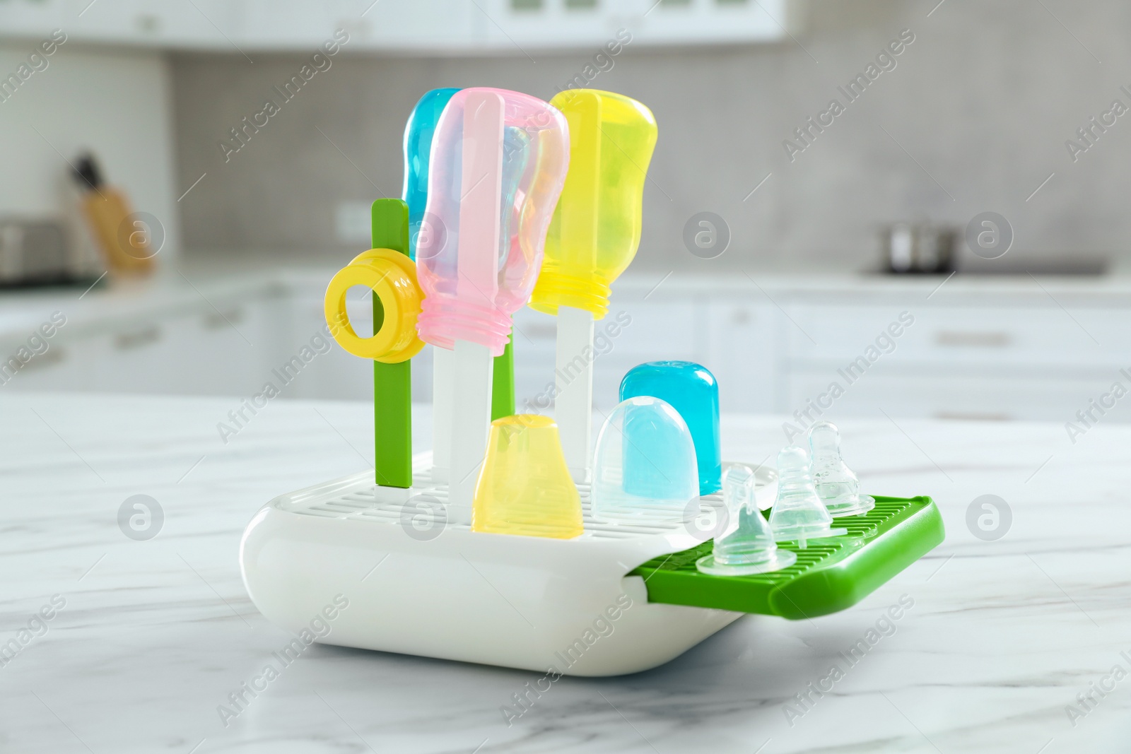 Photo of Dryer with baby bottles and nipples after sterilization on white marble table in kitchen