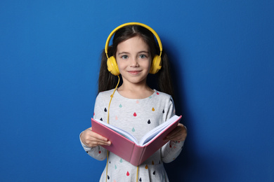 Photo of Cute little girl with headphones listening to audiobook on blue background