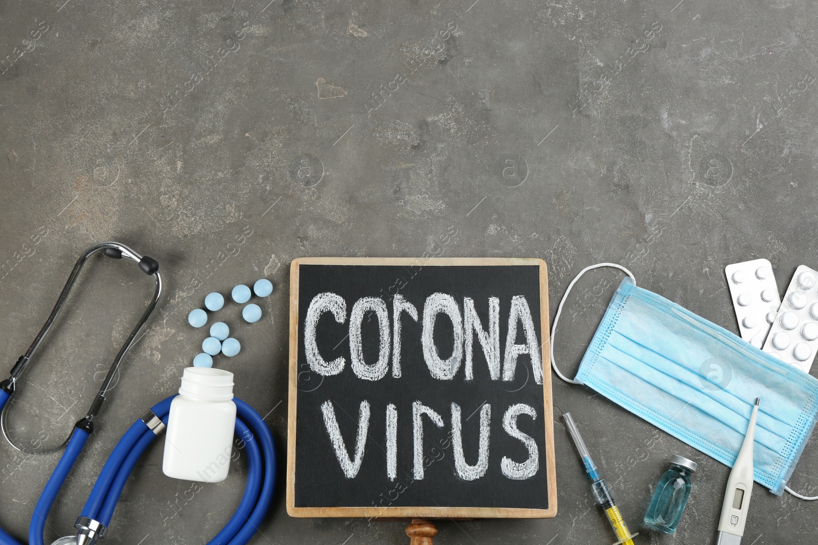Photo of Chalkboard with words CORONA VIRUS, stethoscope and medicines on grey stone background, flat lay. Space for text