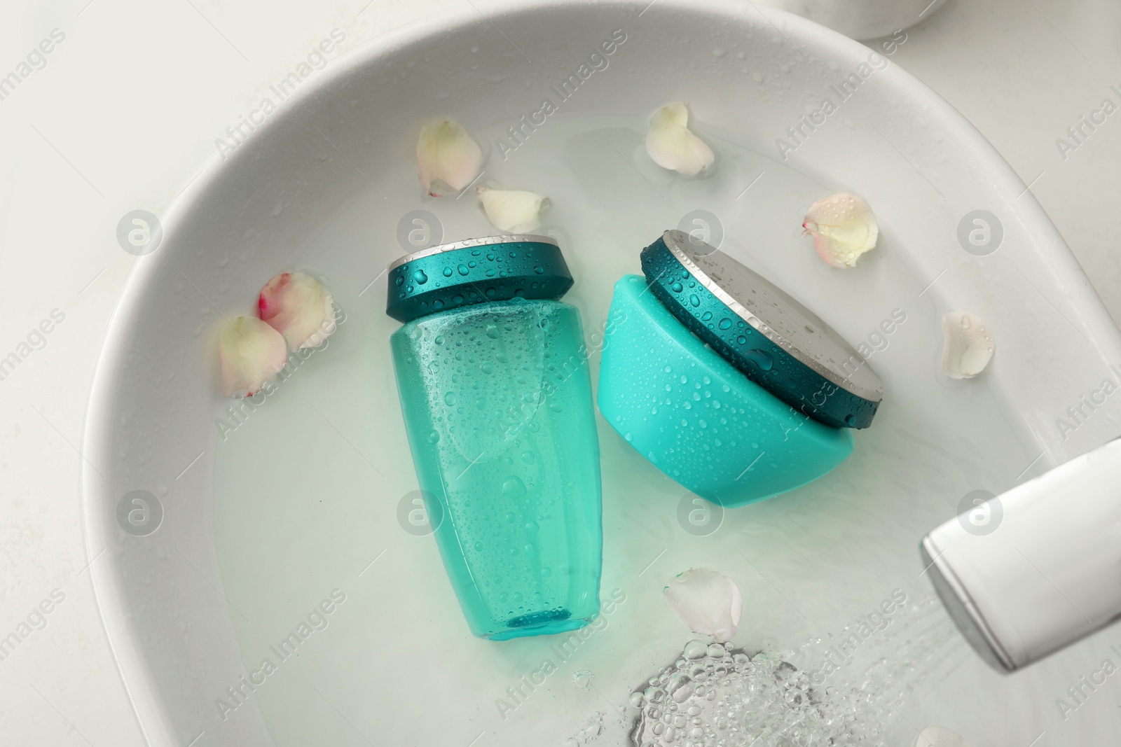 Photo of Hair care cosmetic products with flower petals and water in sink, above view