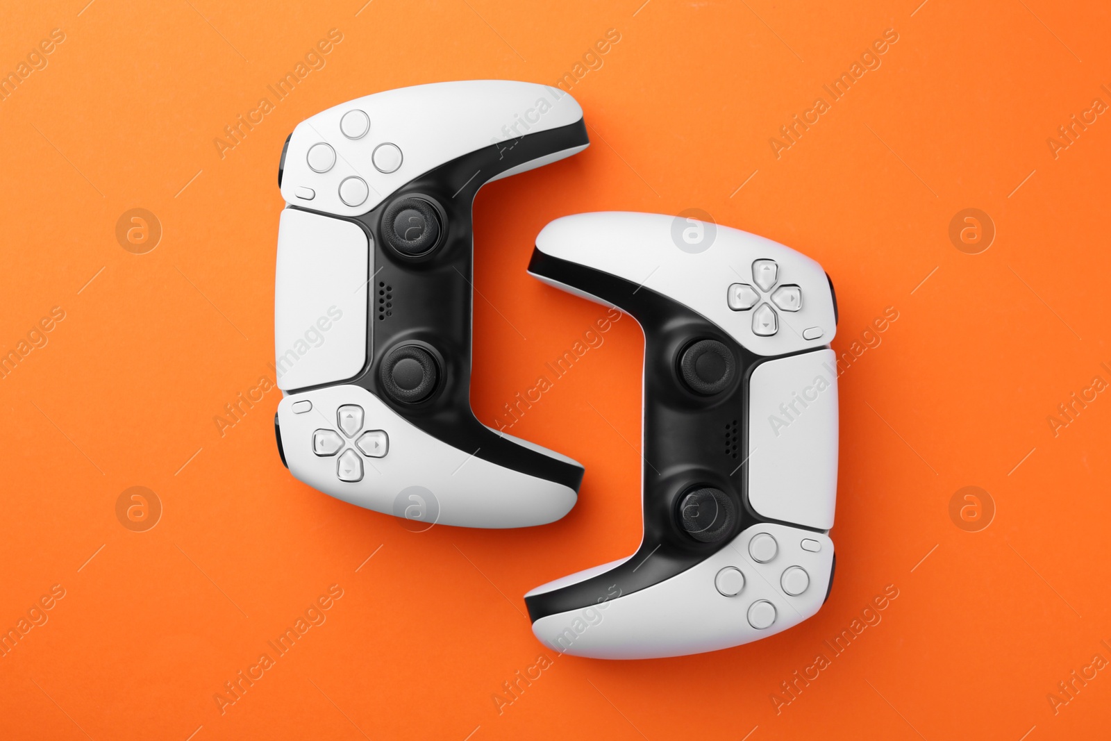 Photo of Wireless game controllers on orange background, flat lay