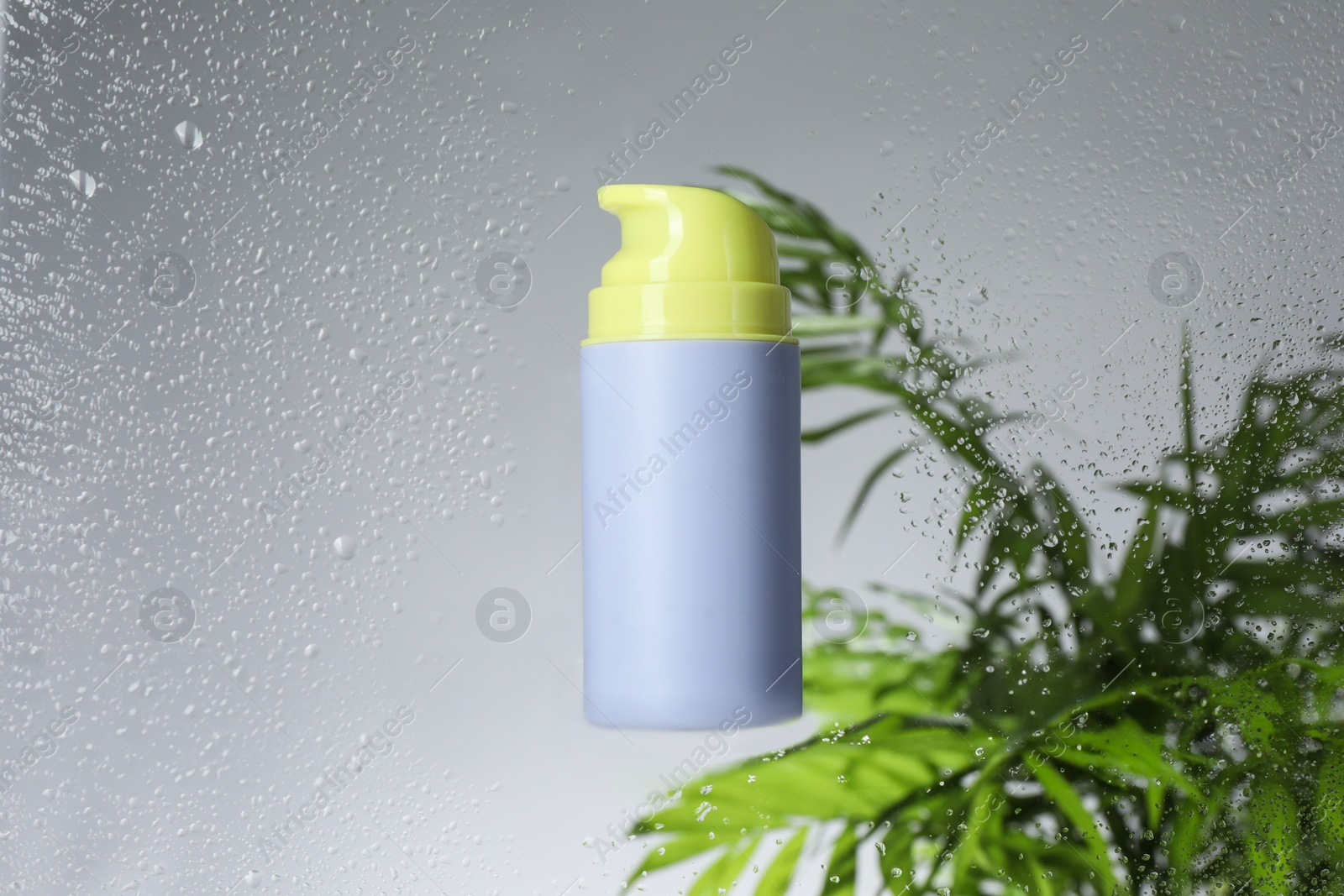 Photo of Bottle with moisturizing cream and palm leaves on light background, view through wet glass. Space for text