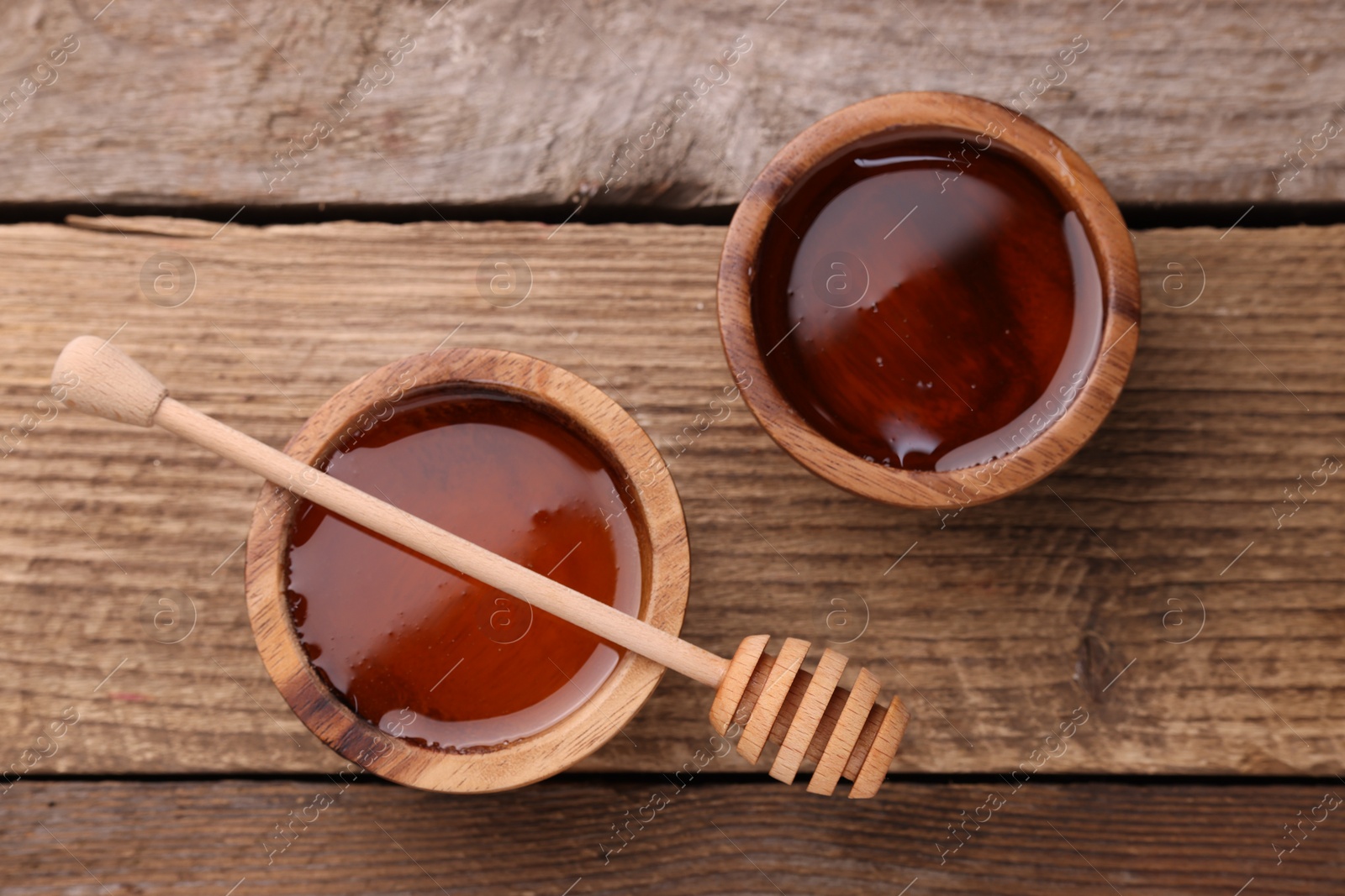 Photo of Delicious honey in bowls and dipper on wooden table, flat lay