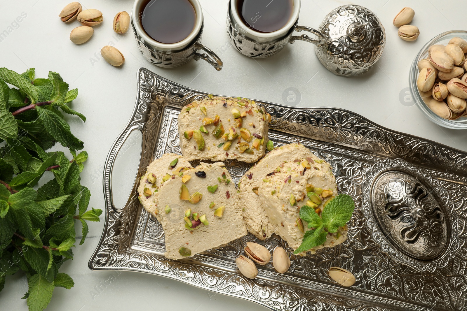 Photo of Tasty halva with pistachios and mint served on light table, flat lay