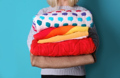 Photo of Woman holding stack of colorful winter clothes on color background