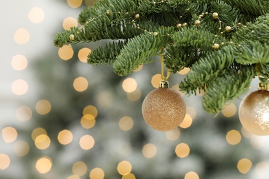 Photo of Golden Christmas balls hanging on fir tree against blurred festive lights