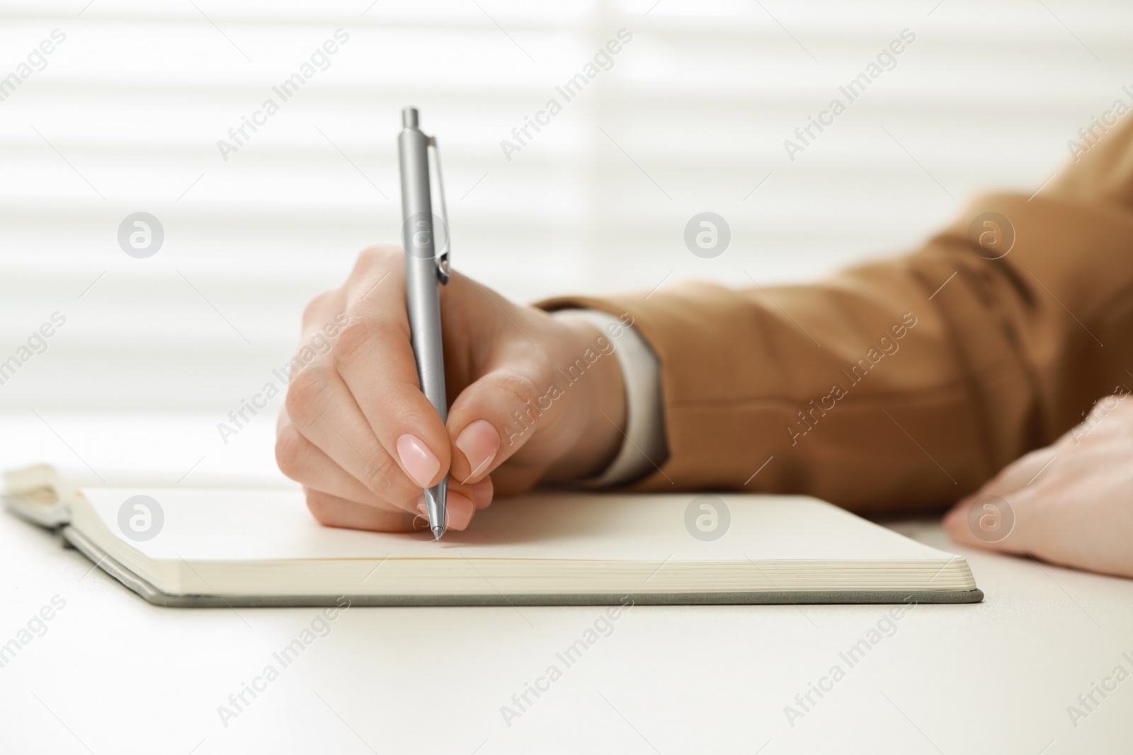 Photo of Woman writing in notebook at white table, closeup