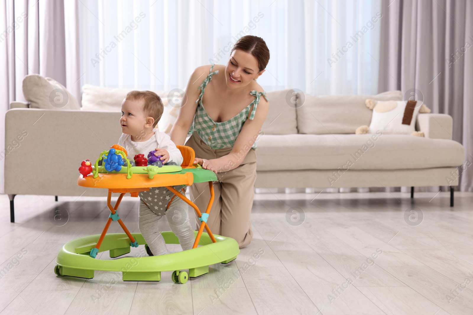 Photo of Cute boy making first steps with baby walker. Happy mother and her little son spending time together at home, space for text