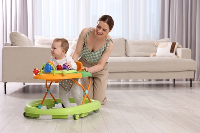 Photo of Cute boy making first steps with baby walker. Happy mother and her little son spending time together at home, space for text