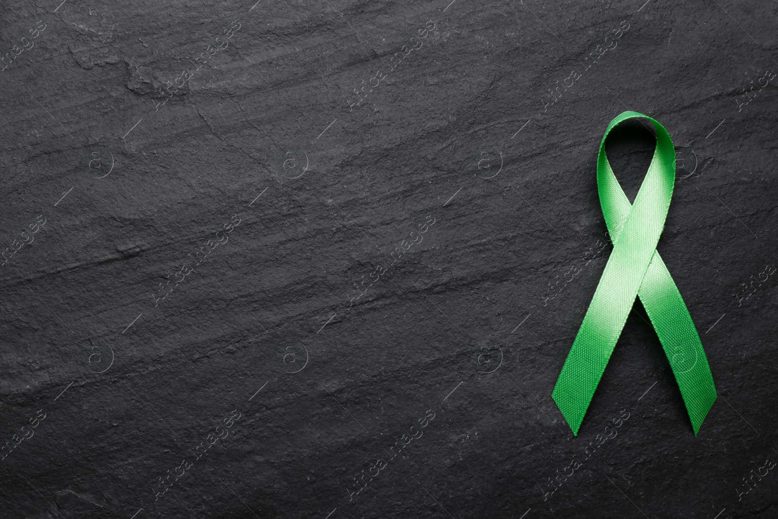 Photo of World Mental Health Day. Green ribbon on black background, top view with space for text