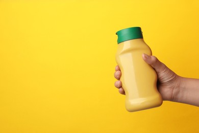 Woman with bottle of mustard on yellow background, closeup. Space for text