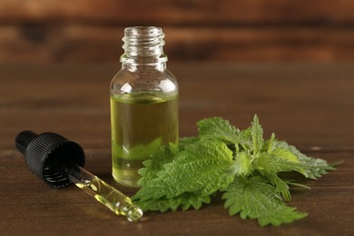 Photo of Fresh nettle leaves near glass bottle and pipette with oil on wooden table, closeup