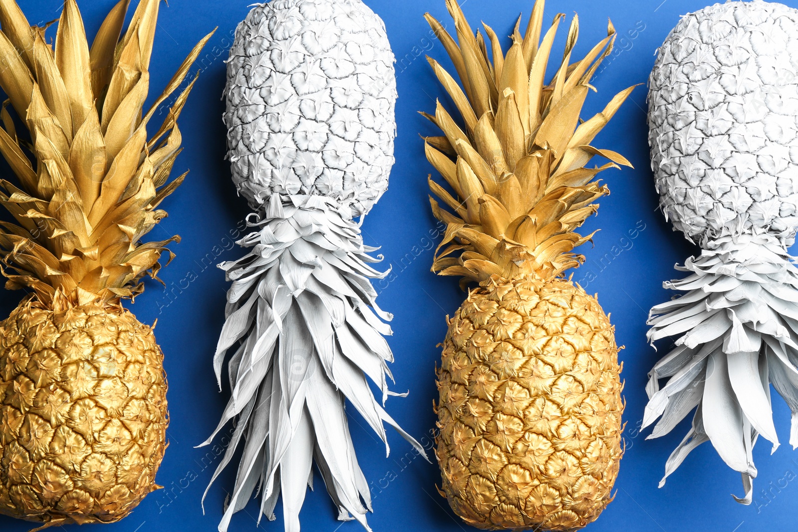 Photo of White and golden pineapples on blue background, flat lay. Creative concept