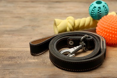 Photo of Black leather dog leash and toys on wooden background, closeup