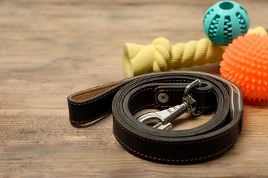 Black leather dog leash and toys on wooden background, closeup