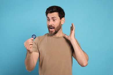Emotional man holding condom on light blue background. Safe sex