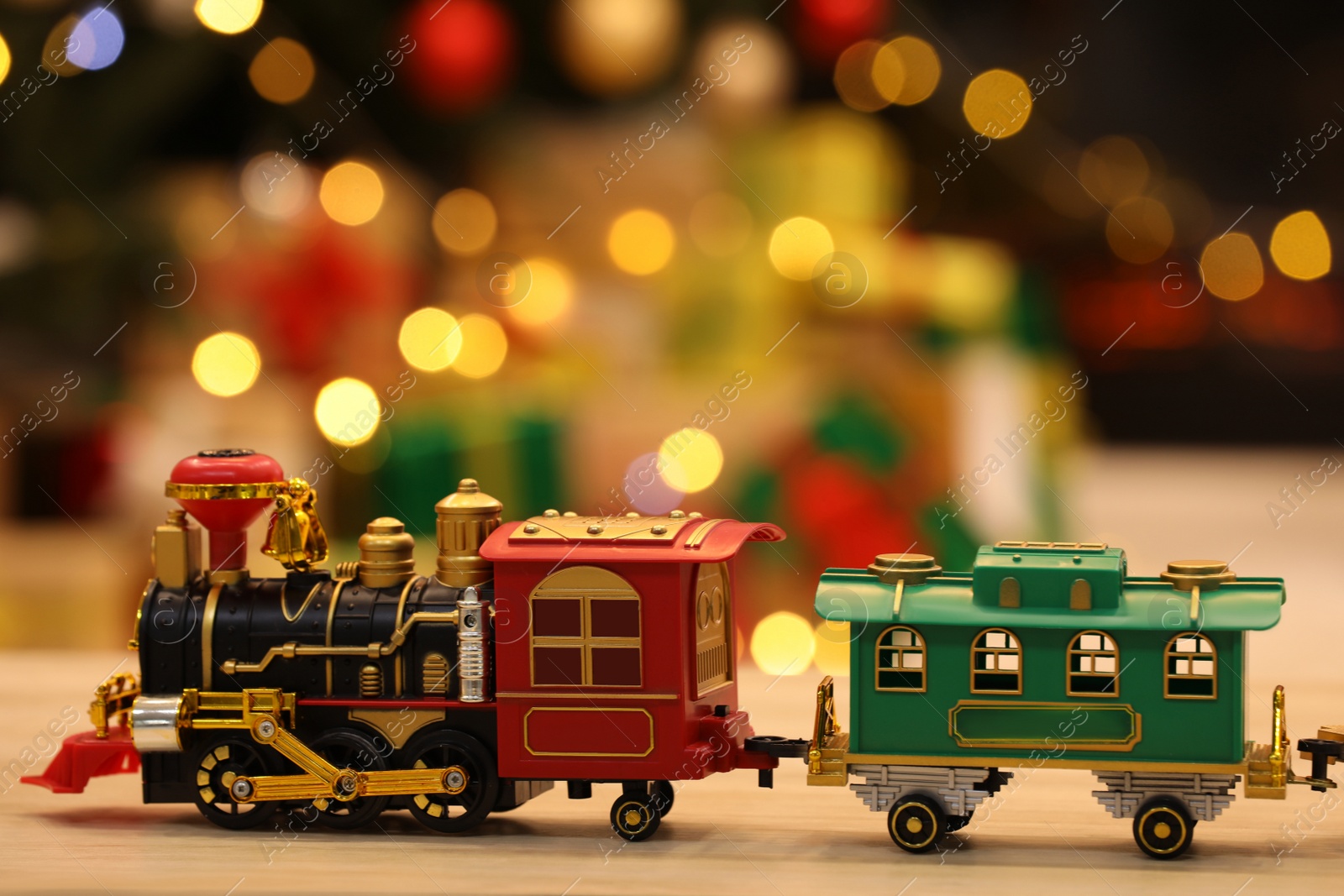 Photo of Beautiful toy train on wooden table against blurred festive lights. Christmas celebration