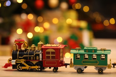Beautiful toy train on wooden table against blurred festive lights. Christmas celebration