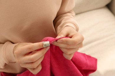 Photo of Woman sewing on red fabric with thimble and needle indoors, closeup. Space for text