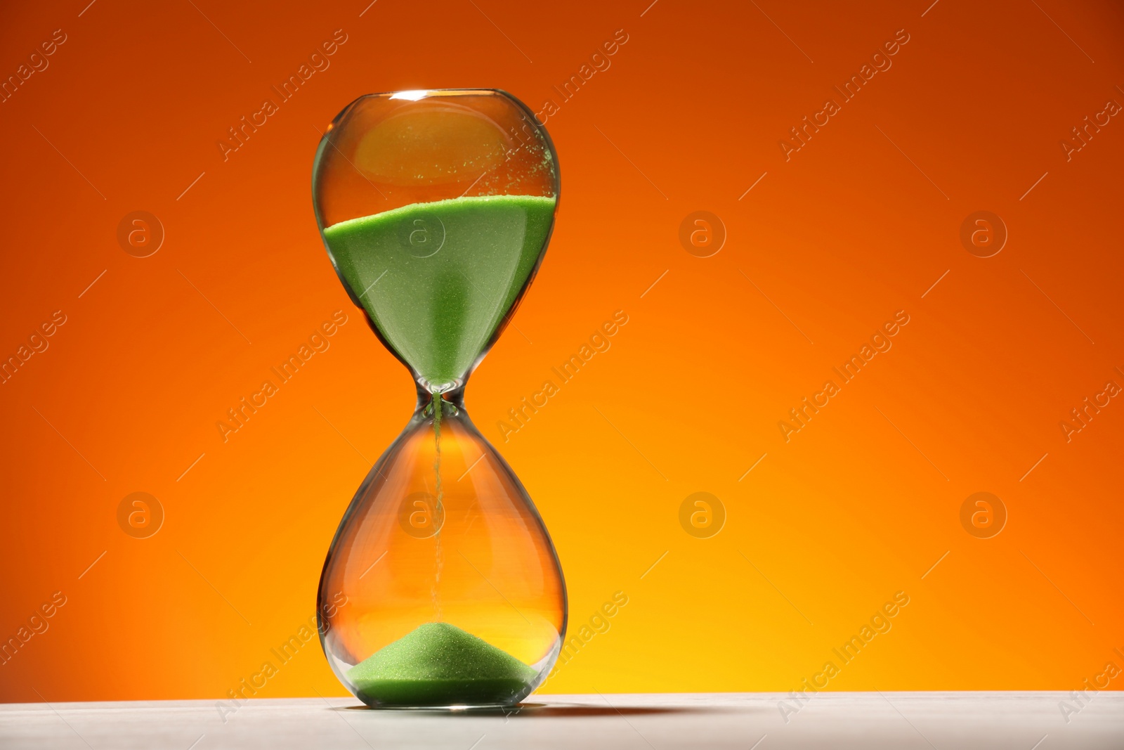 Photo of Hourglass with light green flowing sand on white table against color background. Space for text
