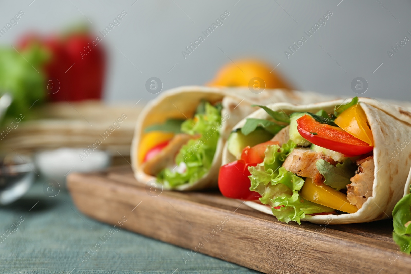 Photo of Board with delicious meat tortilla wraps on blue wooden table against grey background, closeup