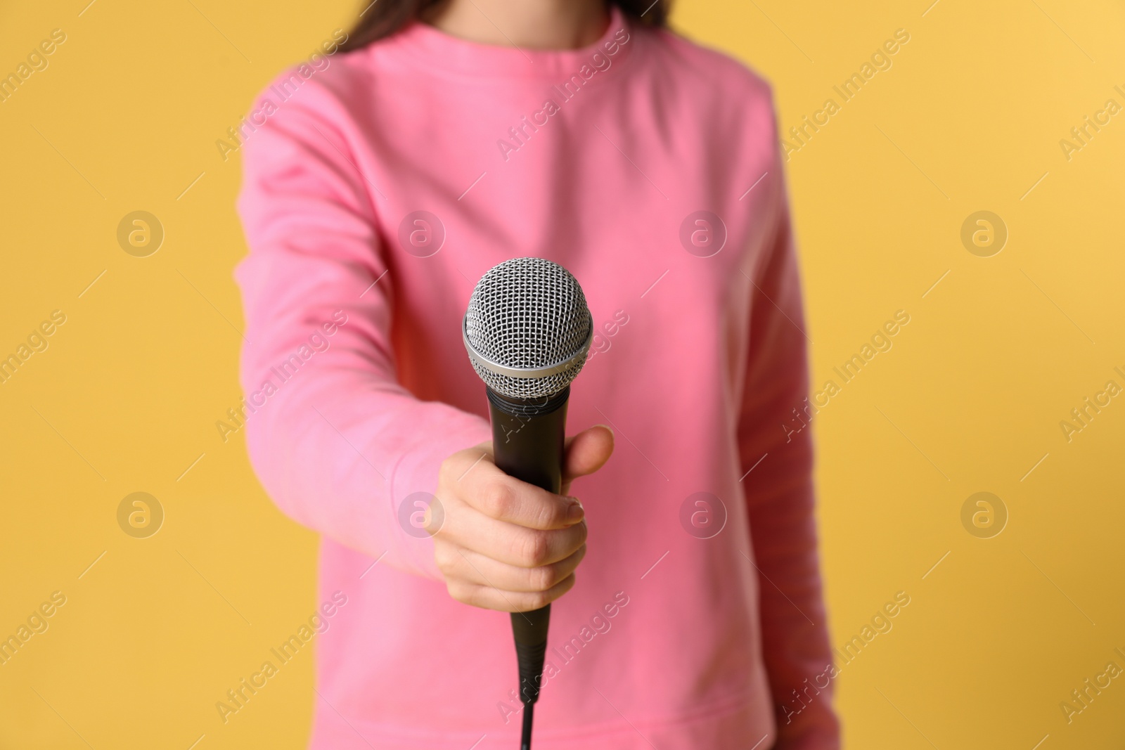 Photo of Young woman holding microphone on color background, closeup view