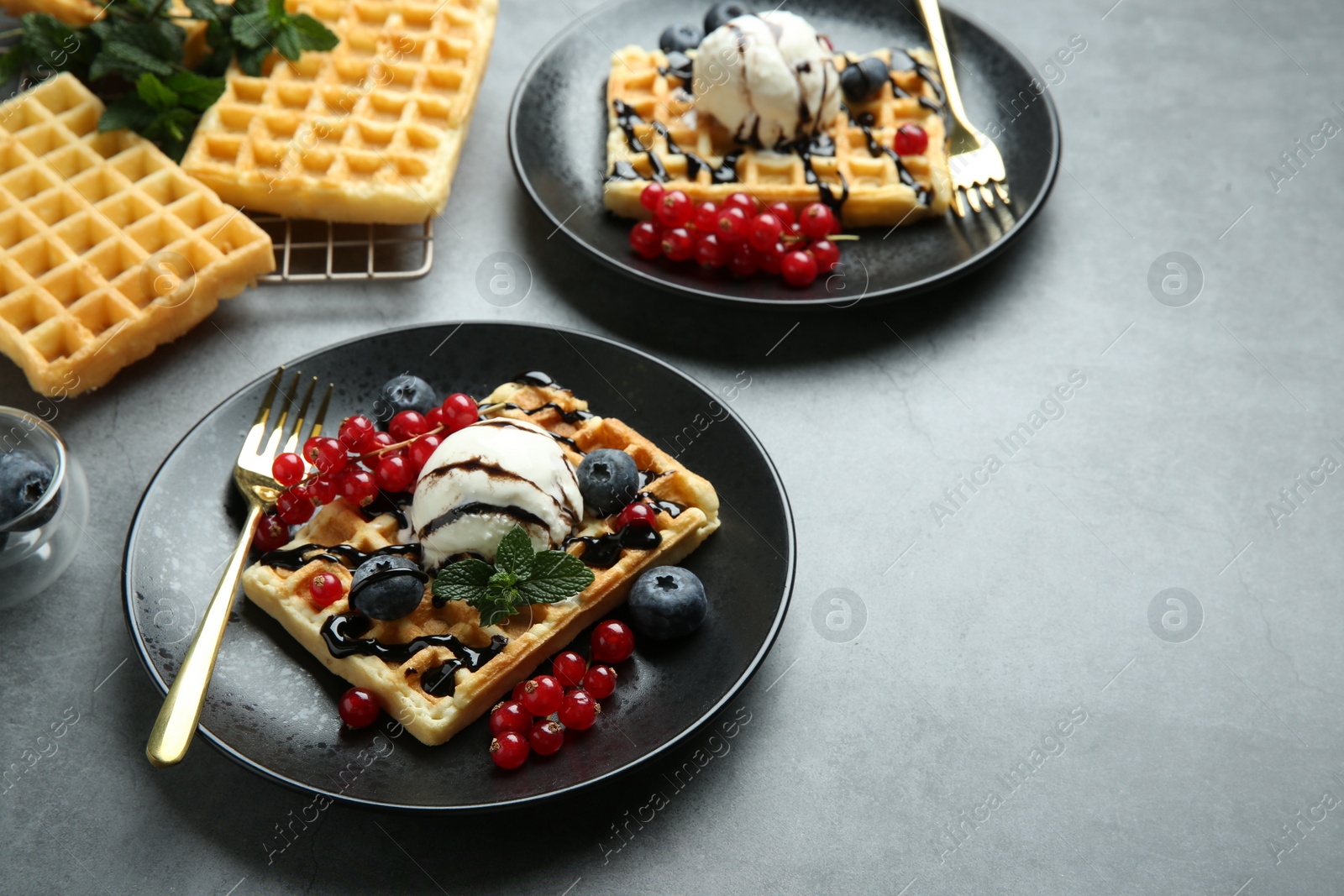 Photo of Delicious Belgian waffles with ice cream, berries and chocolate sauce on grey table. Space for text