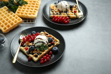 Photo of Delicious Belgian waffles with ice cream, berries and chocolate sauce on grey table. Space for text