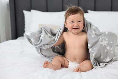 Happy baby boy with blanket sitting on bed at home