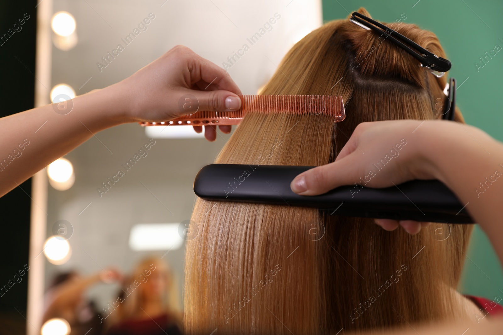 Photo of Stylist straightening woman's hair with flat iron in salon