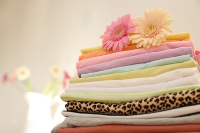 Photo of Stack of clean clothes and flowers on blurred background, closeup. Space for text