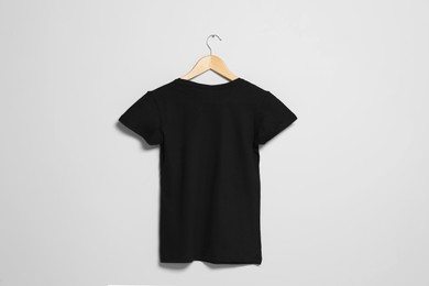 Photo of Hanger with black t-shirt on light wall. Mockup for design