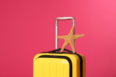 Stylish suitcase with sea star on color background